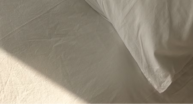 Nahaufnahme von beiger Bettwäsche mit Kissen und sanftem Sonnenlicht – hochwertiges Heimtextilien-Produktbild